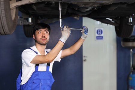 Man technician car mechanic in uniform checking or maintenance a lifted car service at repair garage station. Worker holding wrench and fixing brake discs. Concept of car center repair service.の写真素材
