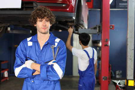 Caucasian technician engineer or worker man uniform standing and holding wrench checking maintenance a car service with confident at repair garage station. Concept of car center repair service.の写真素材
