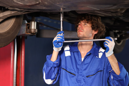 Man technician car mechanic in uniform checking or maintenance a lifted car service at repair garage station. Worker holding wrench and fixing brake discs. Concept of car center repair service.の写真素材