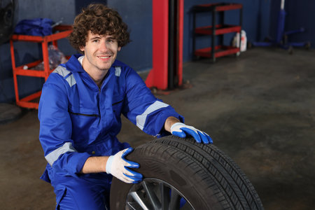 Man technician car mechanic in uniform holding tire for replacement or changeing at repair garage. Happy caucasian worker smiling and looking at camera. Concept of car center repair service.の写真素材