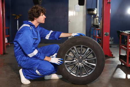 Side view portrait of man technician car mechanic in uniform holding tire for replacement or changeing at repair garage. Concept of car center repair service.の写真素材