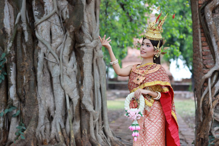 Young fashion and beautiful asian woman wearing Thai red traditional costume holding jasmine flower garland with happy and peace standing outdoor in ancient temple Ayutthaya, Thailand. Travel conceptの写真素材