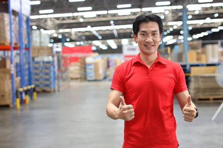 Portrait of warehouse workers young asian man standing and showing thumb up with happy smiling face and confident in retail warehouse logistics, distribution centerの写真素材