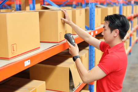 Warehouse workers man with hardhats and reflective jackets scanning barcode on large box package for delivery to production stock and inventory in retail warehouse logistics, distribution centerの写真素材