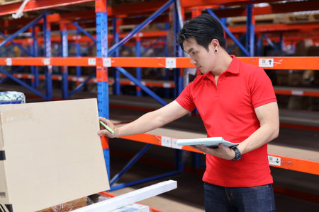 Warehouse workers young asian man working and using tablet, walkie talkie radio and cardboard while controlling stock and inventory in retail warehouse logistics, distribution centerの写真素材