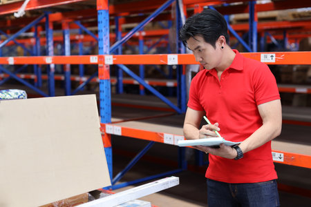 Warehouse workers young asian man working and using tablet, walkie talkie radio and cardboard while controlling stock and inventory in retail warehouse logistics, distribution centerの写真素材