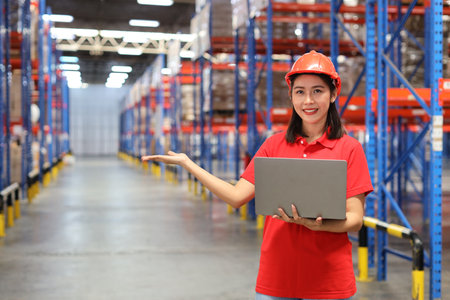 Portrait of warehouse workers young asian woman standing and using computer while posing show something on hand and controlling stock and inventory in retail warehouse logistics, distribution centerの写真素材