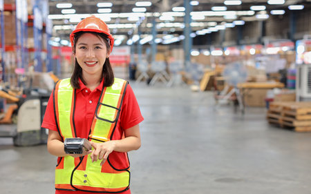 Warehouse workers woman with hardhats and reflective jackets while holding scanner barcode and looking at camera with production stock and retail warehouse logistics distribution center backgroundの写真素材