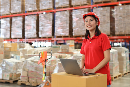 Portrait of warehouse workers young asian woman standing and using computer while looking at camera and controlling stock and inventory in retail warehouse logistics, distribution centerの写真素材