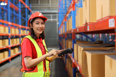 Warehouse workers woman with hardhats and reflective jackets scanning barcode on large box package for delivery to production stock and inventory in retail warehouse logistics, distribution centerの写真素材