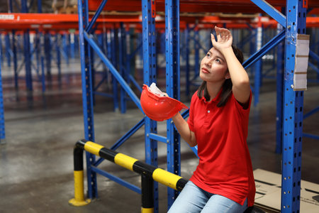 Portrait of warehouse workers young asian woman sitting and taking a break while wipe the sweat away after controlling stock and inventory in retail warehouse logistics, distribution centerの写真素材