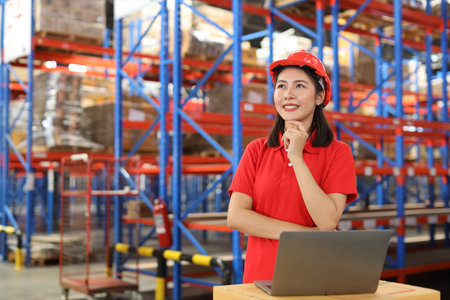 Portrait of warehouse workers young asian woman standing and using computer while looking away while controlling stock and inventory in retail warehouse logistics, distribution centerの写真素材