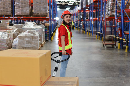 Warehouse worker woman with hardhats and reflective jackets pulling a pallet truck and taking or upload with large box package to shelf in retail warehouse logistics, distribution centerの写真素材