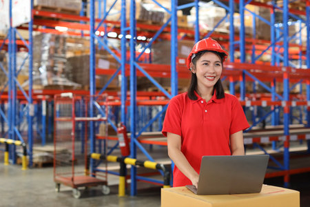 Portrait of warehouse workers young asian woman standing and using computer while looking at camera and controlling stock and inventory in retail warehouse logistics, distribution centerの写真素材