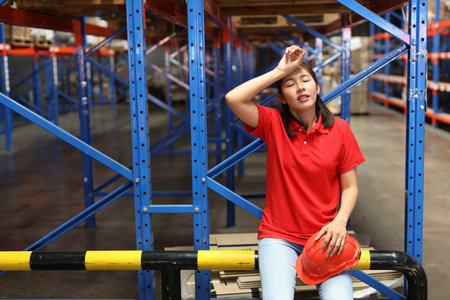Portrait of warehouse workers young asian woman sitting and taking a break while wipe the sweat away after controlling stock and inventory in retail warehouse logistics, distribution centerの写真素材