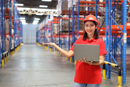 Portrait of warehouse workers young asian woman standing and using computer while posing show something on hand and controlling stock and inventory in retail warehouse logistics, distribution centerの写真素材