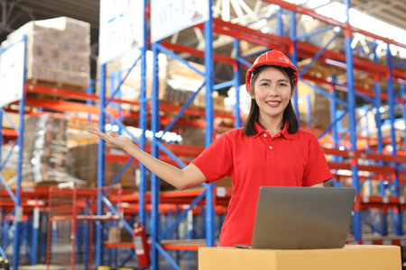 Portrait of warehouse workers young asian woman standing and showing something on hand while looking at camera and controlling stock and inventory in retail warehouse logistics, distribution centerの写真素材