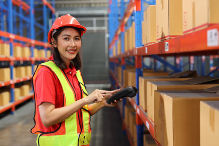 Warehouse workers woman with hardhats and reflective jackets scanning barcode on large box package for delivery to production stock and inventory in retail warehouse logistics, distribution centerの写真素材
