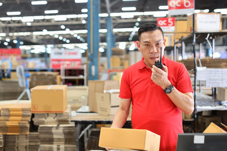 Warehouse workers man using computer, walkie talkie radio and cardboard for controlling stock and payment in retail warehouse logistics, distribution centerの写真素材