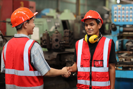 Happy smiling teamwork technician engineer or worker in protective uniform with hardhat shaking hands celebrate successful together completed deal commitment at heavy industry manufacturing factoryの写真素材