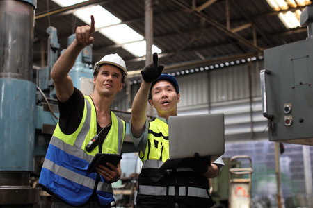 Architect men and worker checking and pointing at heavy industry manufacturing factory with computer. Multiethnic business manager looking in future with warehouse factory buildingの写真素材