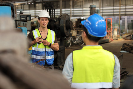 Technician engineer in protective uniform with hardhat standing and teaching apprentices or colleague worker to use computerized machine control at heavy industry manufacturing factoryの写真素材