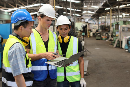 Architect men and worker checking and pointing at heavy industry manufacturing factory with computer. Multiethnic business manager looking in future with warehouse factory buildingの写真素材