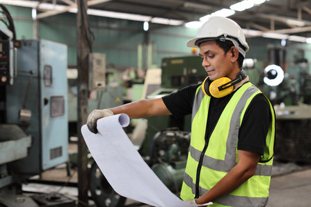 Architect man or worker standing and checking at heavy industry manufacturing factory with blueprint. Asian business manager looking in future with warehouse factory buildingの写真素材