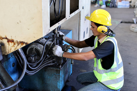 Technician engineer or worker in protective uniform standing and repairing operation or checking industry machine process with safety hardhat at heavy industry manufacturing factoryの写真素材