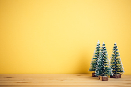 Snow covered pine trees on wooden table with yellow backgroundの写真素材