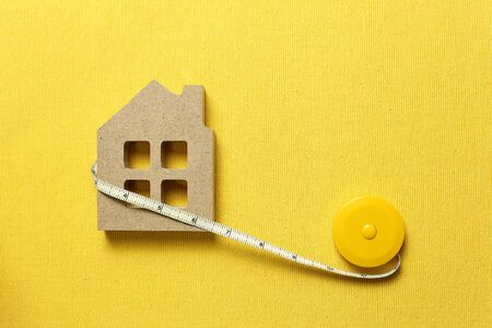 House model with tape measure on yellow fabric background. Buying a house, house size, real estate conceptの写真素材