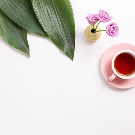 Cup of black tea with green leaves and flowers on white background. Flat lay, top view, copy spaceの写真素材