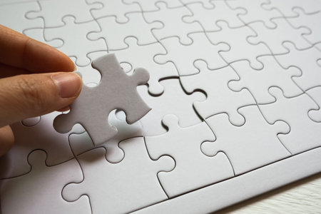 Set of white puzzle pieces and hand holding last one piece