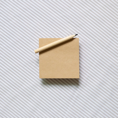 Brown kraft memo pad, empty paper with wooden pencil on gray stripe pattern fabric background. top...