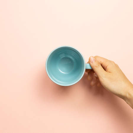 Female hand holding blue empty mug cup on pink background. top viewの写真素材