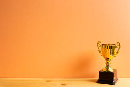 Champion golden trophy on wooden table with orange backgroundの写真素材