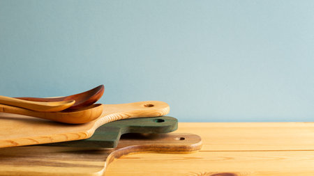 Wooden tray, cutting board, plate and spoons on wooden table with blue background