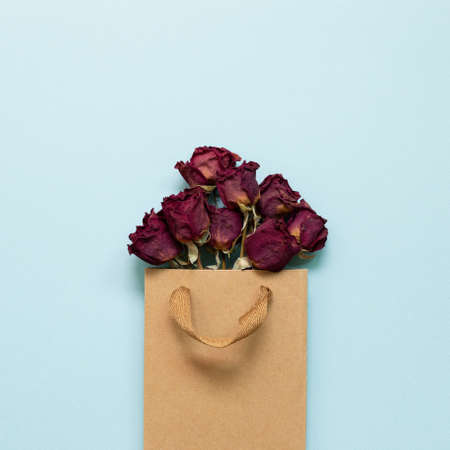 Dry rose flowers in kraft shopping bag on blue background. top view, copy spaceの写真素材