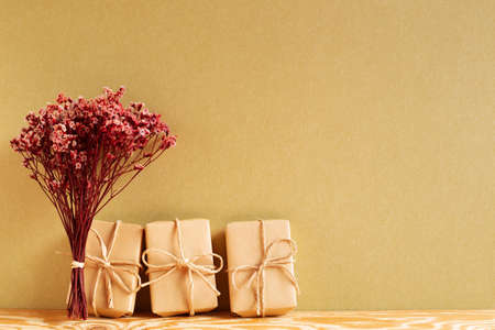 Gift boxes with red sinensis dry flower bouquet on wooden table with khaki brown backgroundの写真素材