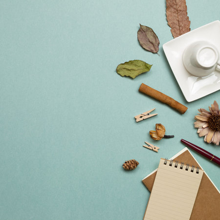 Autumn concept. Notebook and mug cup with dry leaves on green background. flat lay, top view, copy...