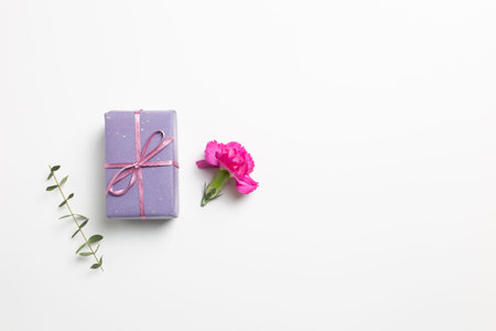 Purple gift box with carnation flower on white background. flat lay, top view, copy space