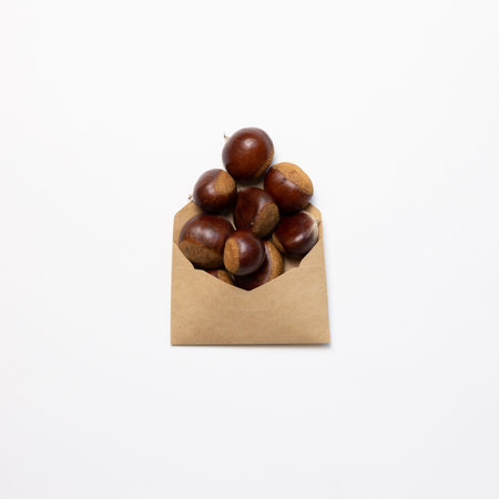 Chestnuts in a paper bag on white background. Autumn and winter snacks. top view, copy space