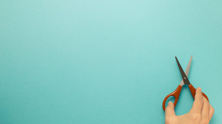 Scissors with hand on blue background. top view, copy space