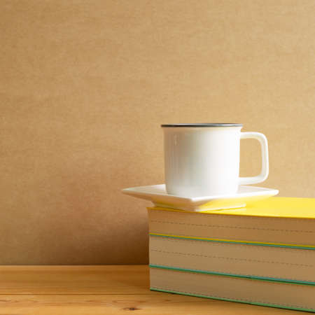 Books with cup of coffee on wooden desk with brown backgroundの写真素材