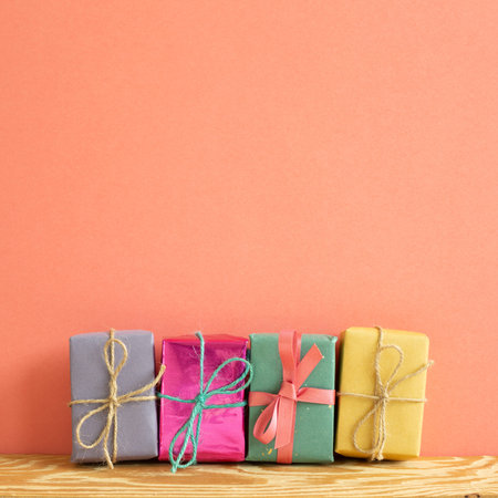 Colorful gift boxes on wooden table with coral pink background