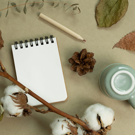 Winter and autumn concept. Notebook, mug cup, colored pencil, cotton plant, dry leaves on khaki...