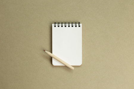Empty memo note pad with wooden pencil on khaki brown paper background. top view, copy space