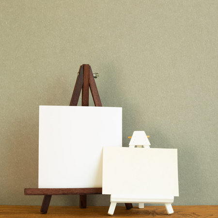 Easel with blank canvas on wooden desk. Khaki green background
