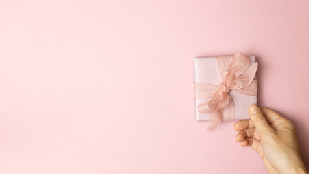 Hand holding pink gift box on pink background. top view, copy spaceの写真素材