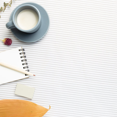 Work and study place. Notebook, cup of milk, pencil with dry plant on stripe pattern fabric...